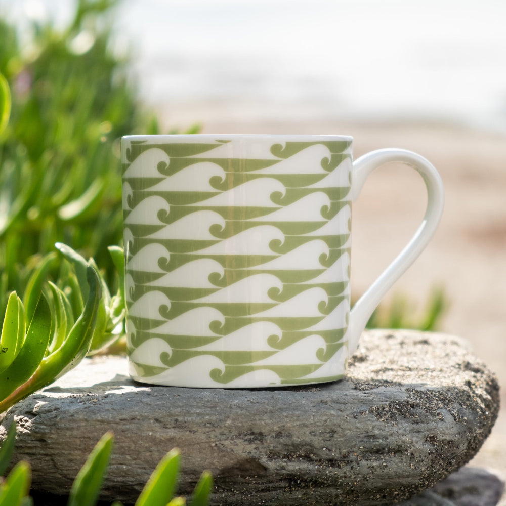 Green and white patterned wave mug on a rock with greenery in the background