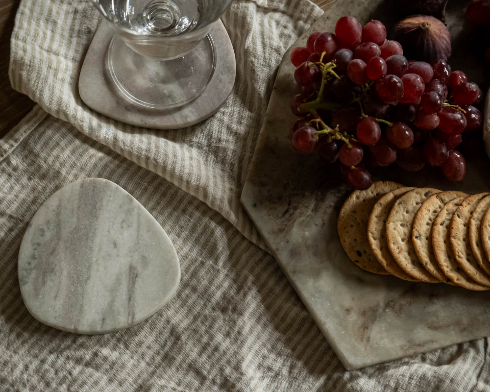 Glasses, grapes, and crackers on a textured tablecloth with marble coasters