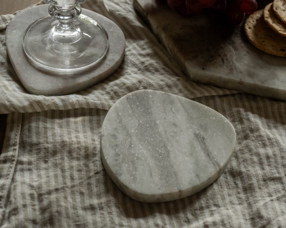 Marble coaster on a textured fabric surface with a glass and bread slices in the background.