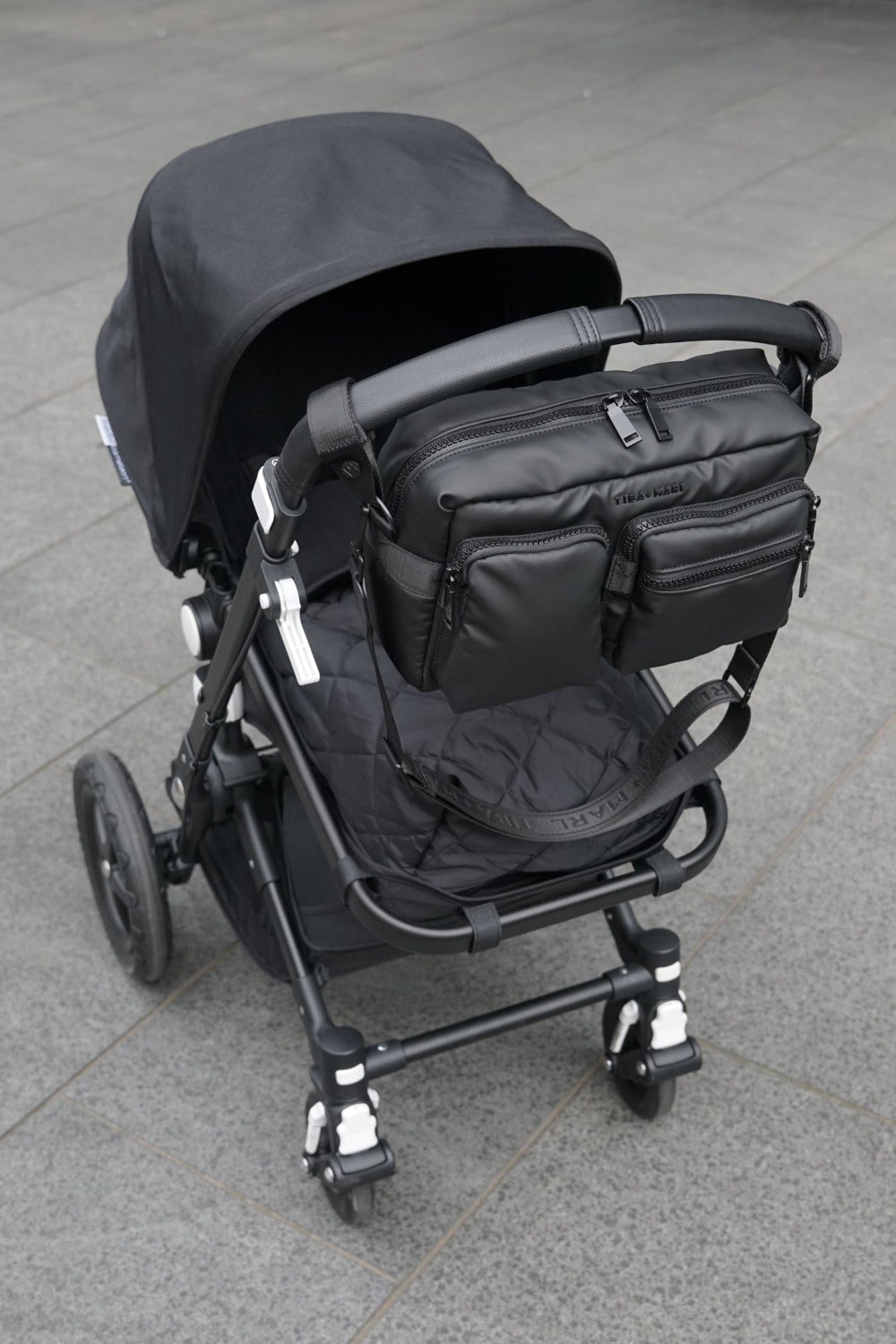 Black stroller with a Axel Black crossbody bag attached on a grey pavement