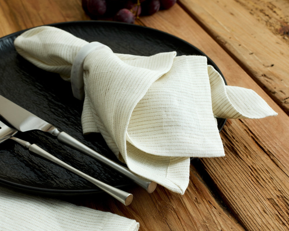 White napkin folded on a black plate with cutlery on a wooden table