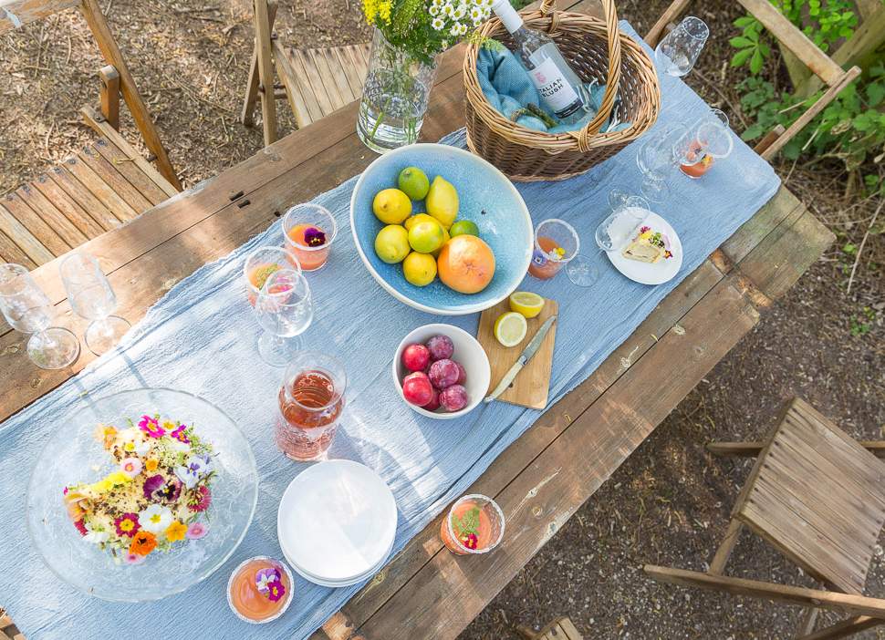 Outdoor table setting with fruit, drinks, and snacks on a wooden table.