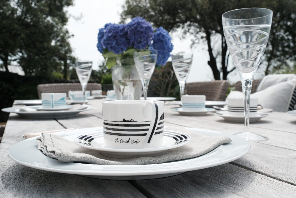 Dining table set with white plates, blue flowers, and decorative items on a wooden deck.