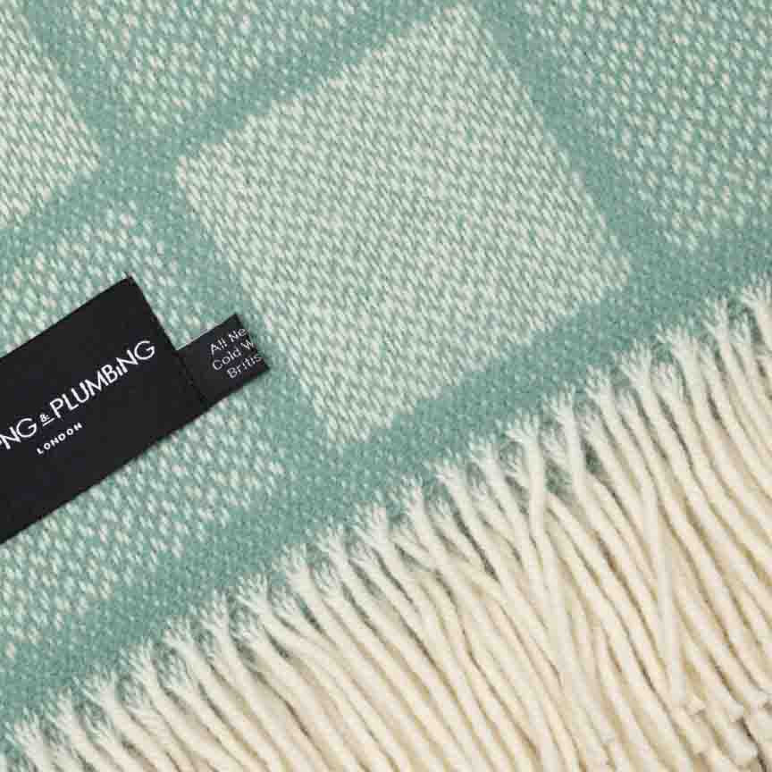Teal and white checkered blanket with a brand tag on a light green background
