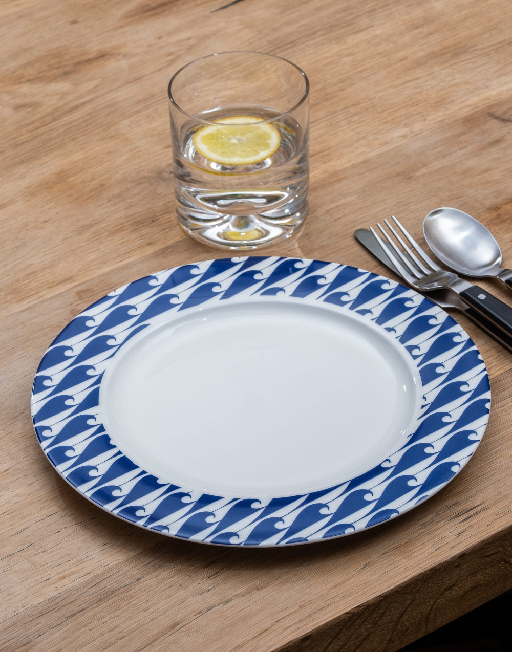 White plate with blue wave pattern on a wooden table with a glass of water and lemon.
