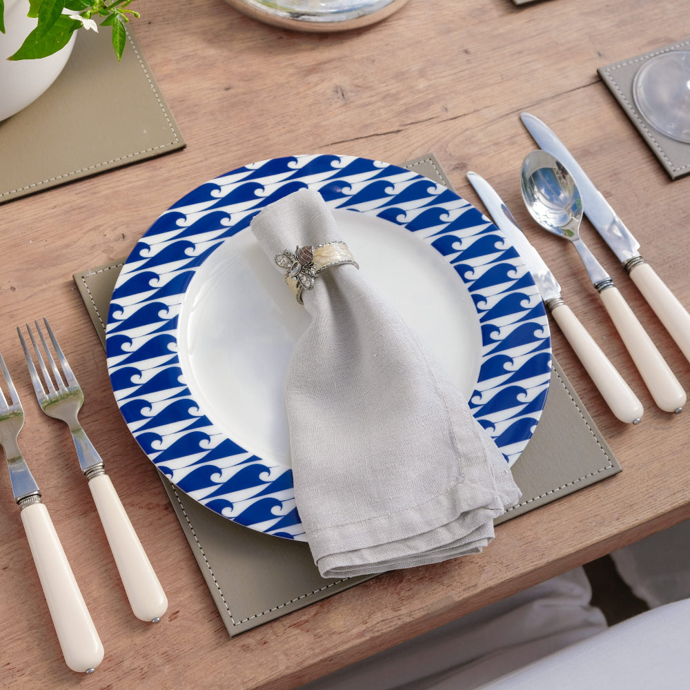 Table setting with blue and white wave patterned plate, silverware, and napkin on a wooden table.