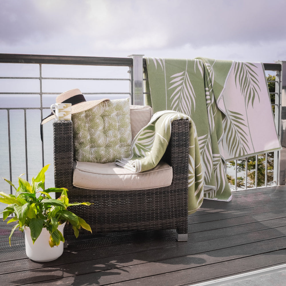 Chair with patterned cushions and a green botanical leaf blanket on a wooden deck