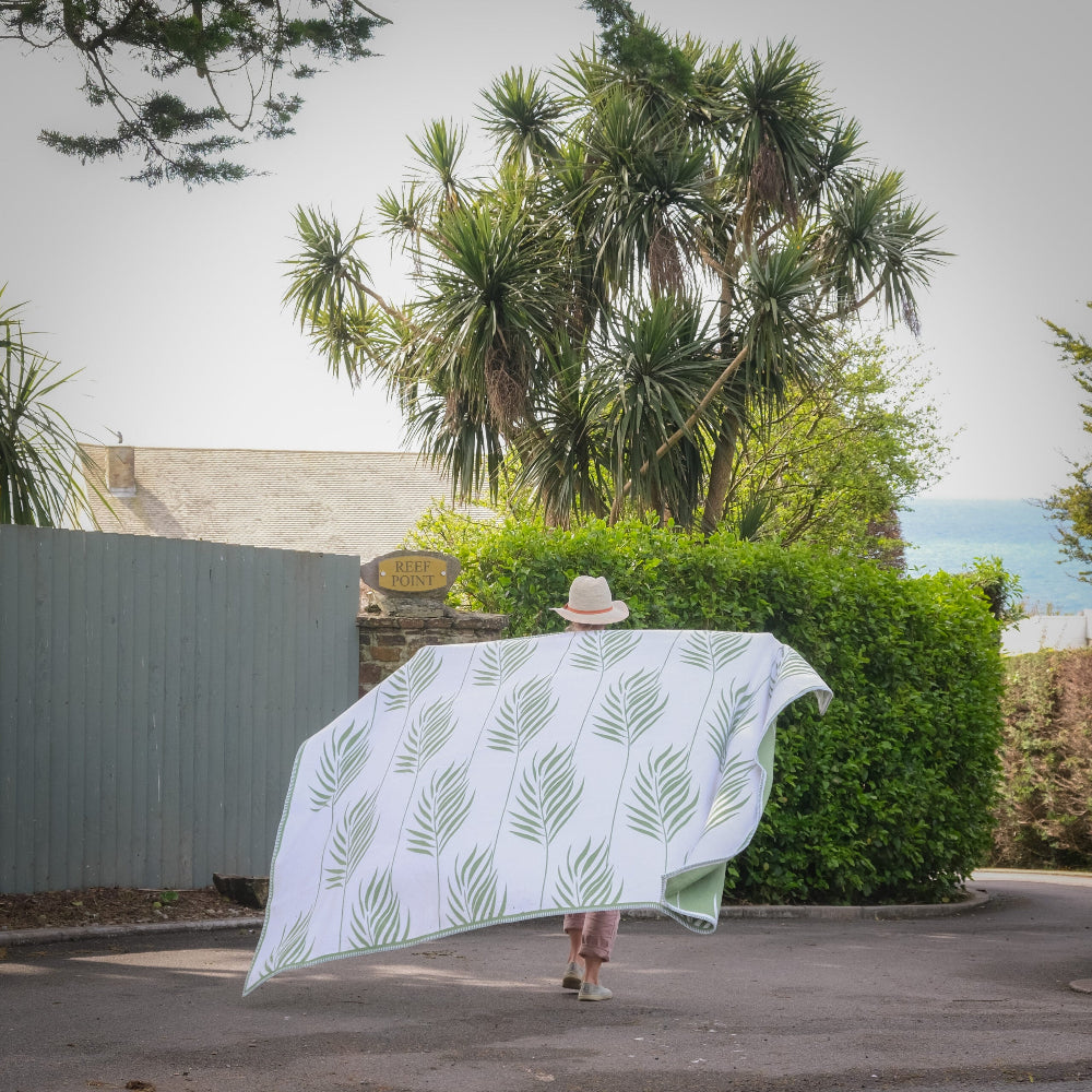 Person holding a large white and green blanket with green leaf patterns in an outdoor setting.