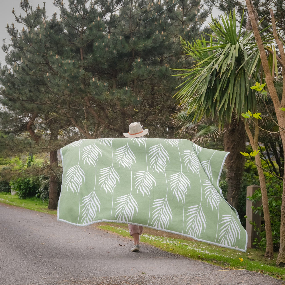 Person holding a green blanket with white leaf pattern in a park setting