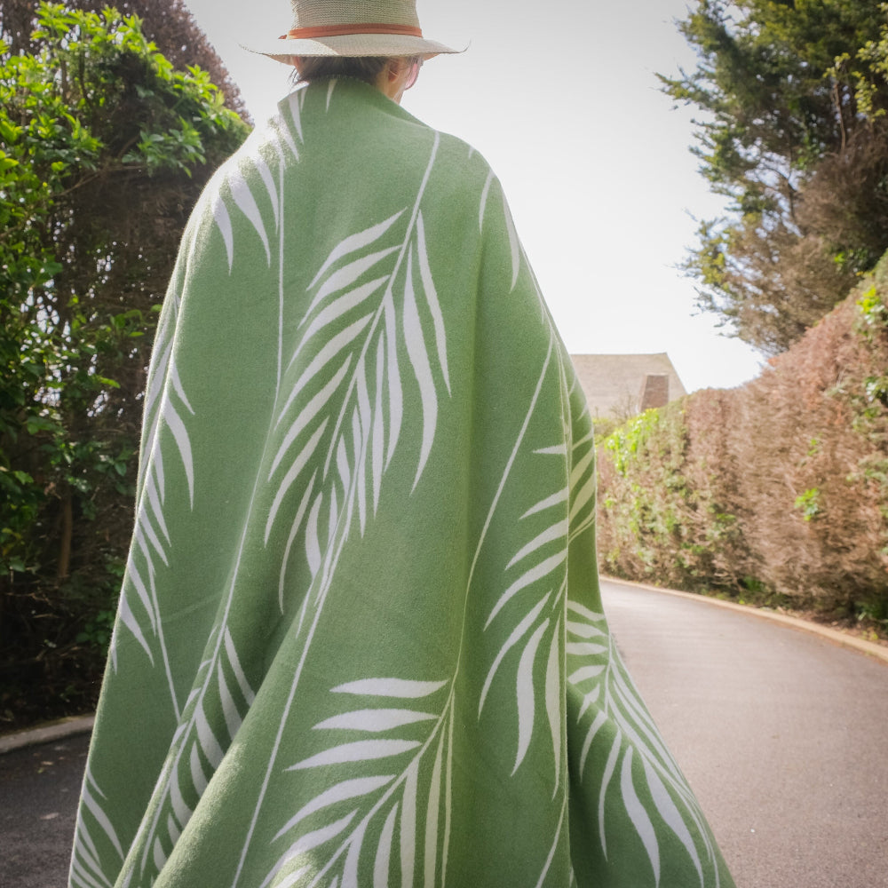 Person walking on a path wearing a green blanket with white leaf patterns