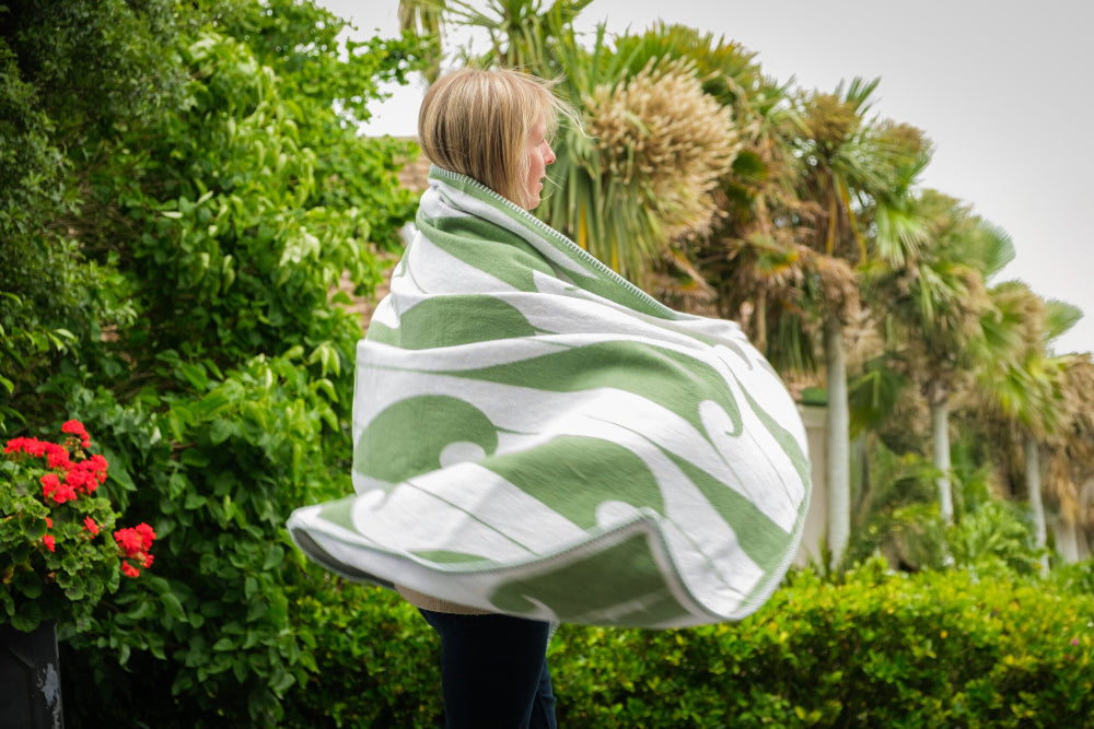Person wrapped in a green and white patterned blanket outdoors with plants and flowers in the background