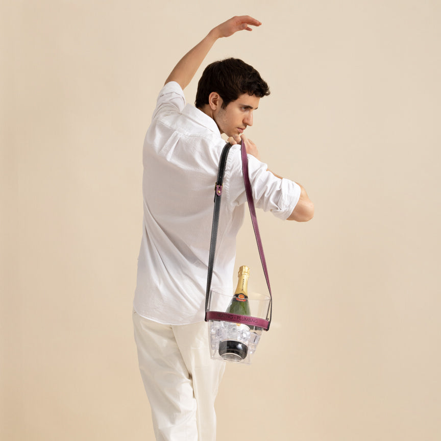 Man holding a transparent bag with a bottle of champagne against a beige background
