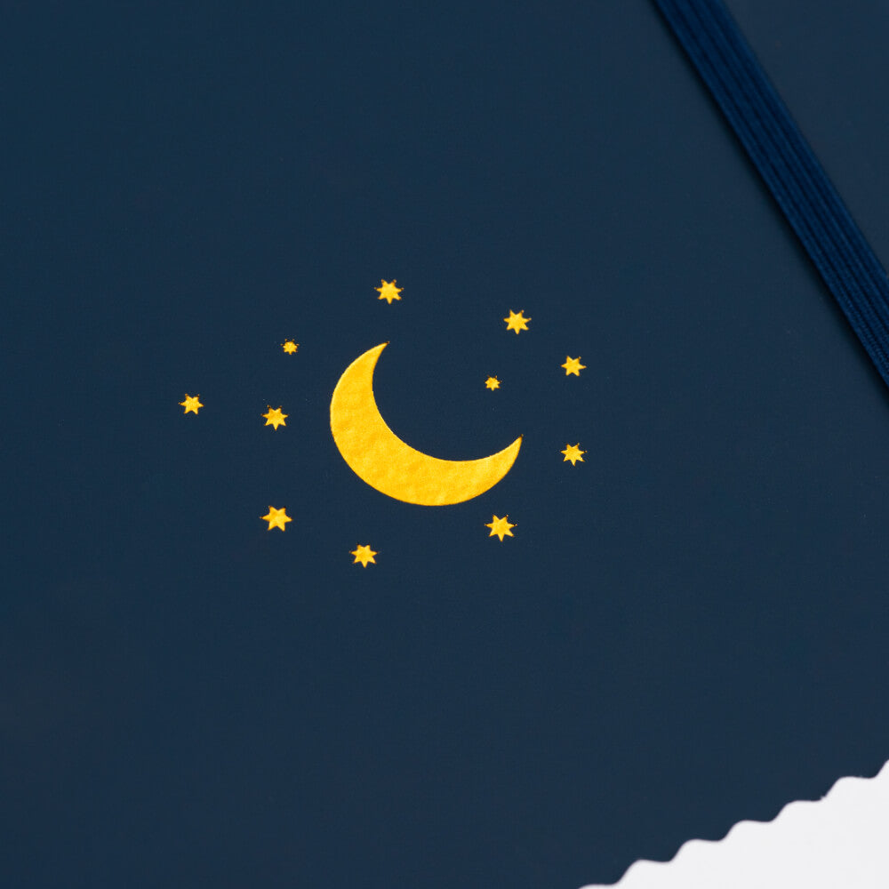 Closeup of Yop & Tom Midnight blue A5 Journal showing the Yellow crescent moon and stars on a dark blue background