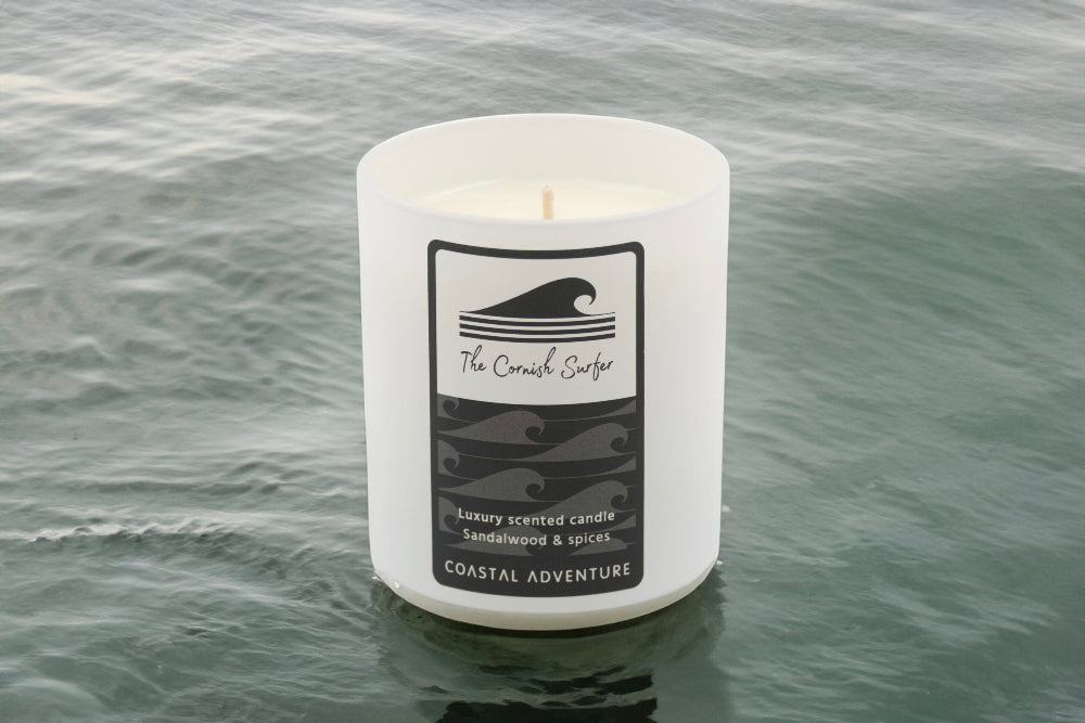 Candle with a label in water, featuring 'The Cornish Surfer' brand.
