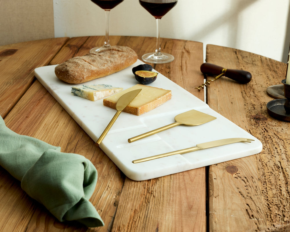 Cheeseboard with assorted cheeses, bread, and wine glasses on a wooden table.