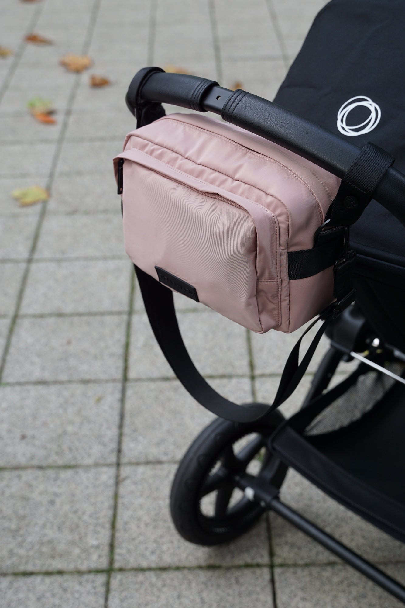 Pink stroller organizer attached to a black stroller on a tiled pavement.