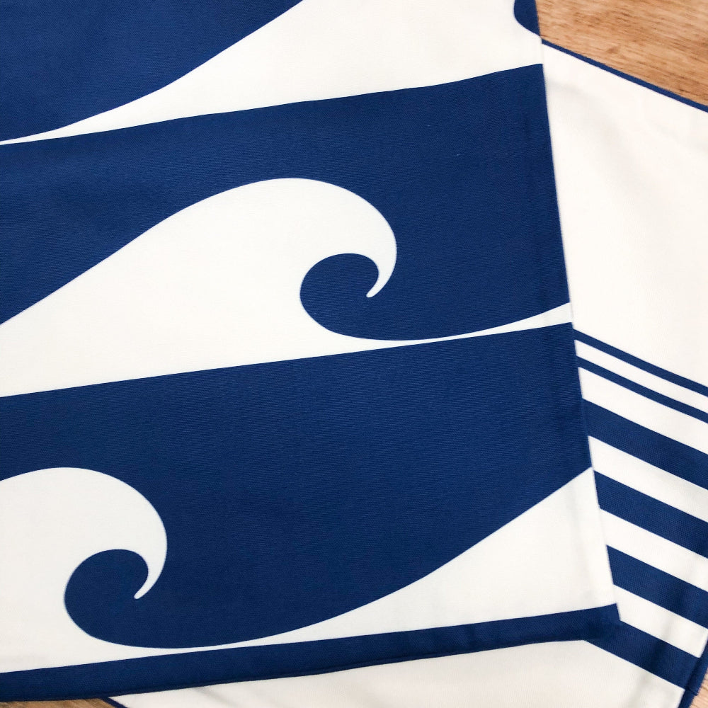 Nautical-themed cushion cover with wave design and stripes on a wooden surface