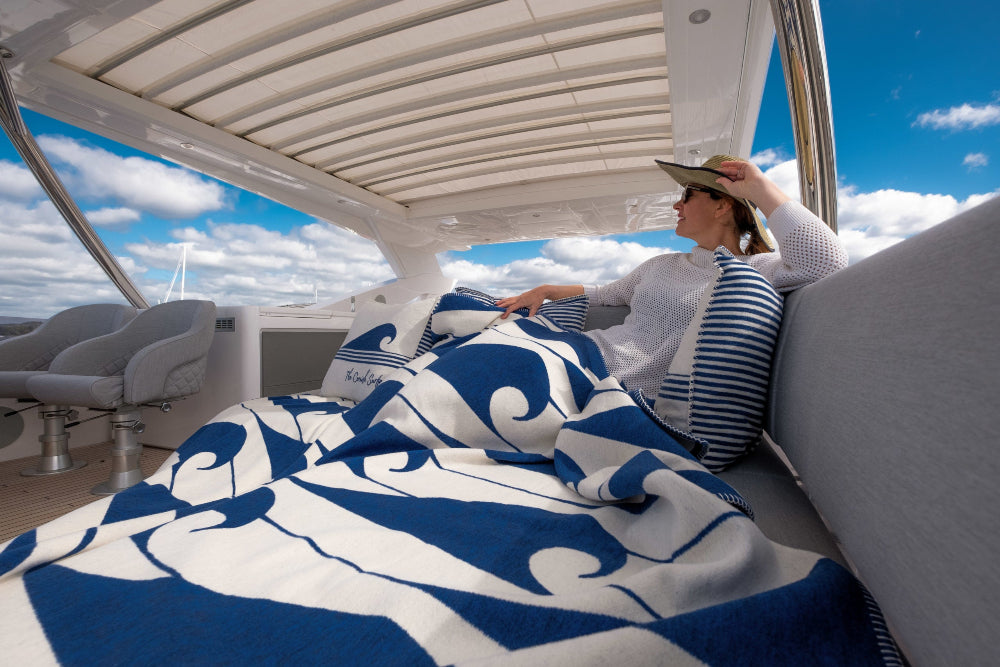 Person sitting on a boat with a blue and white patterned blanket, surrounded by water and sky.