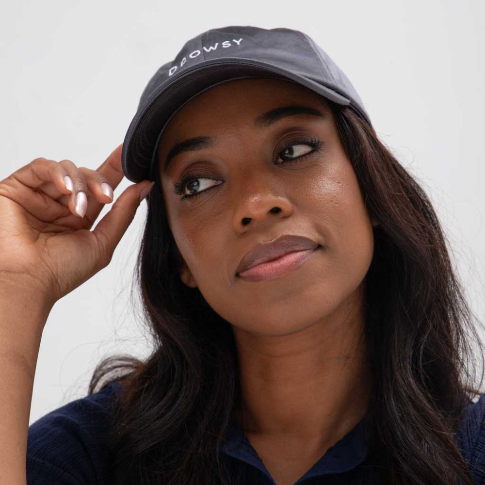 Woman wearing a cap with 'Drowsy' branding against a plain background
