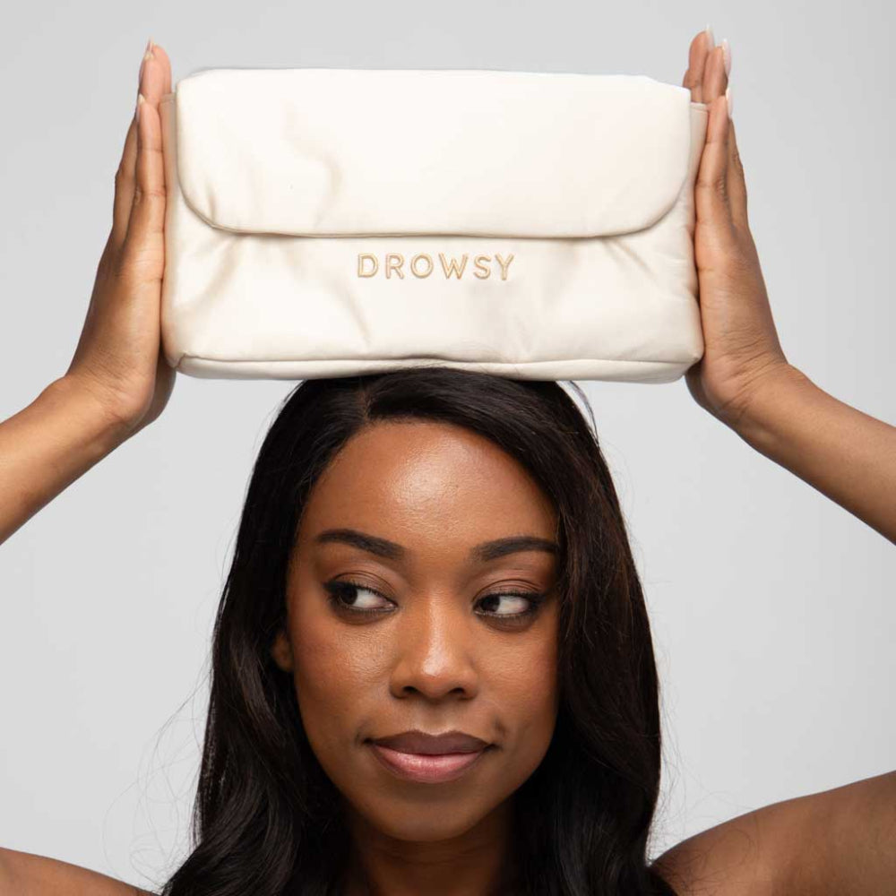 Woman holding a Gold pouch with 'Drowsy' branding above her head against a grey background