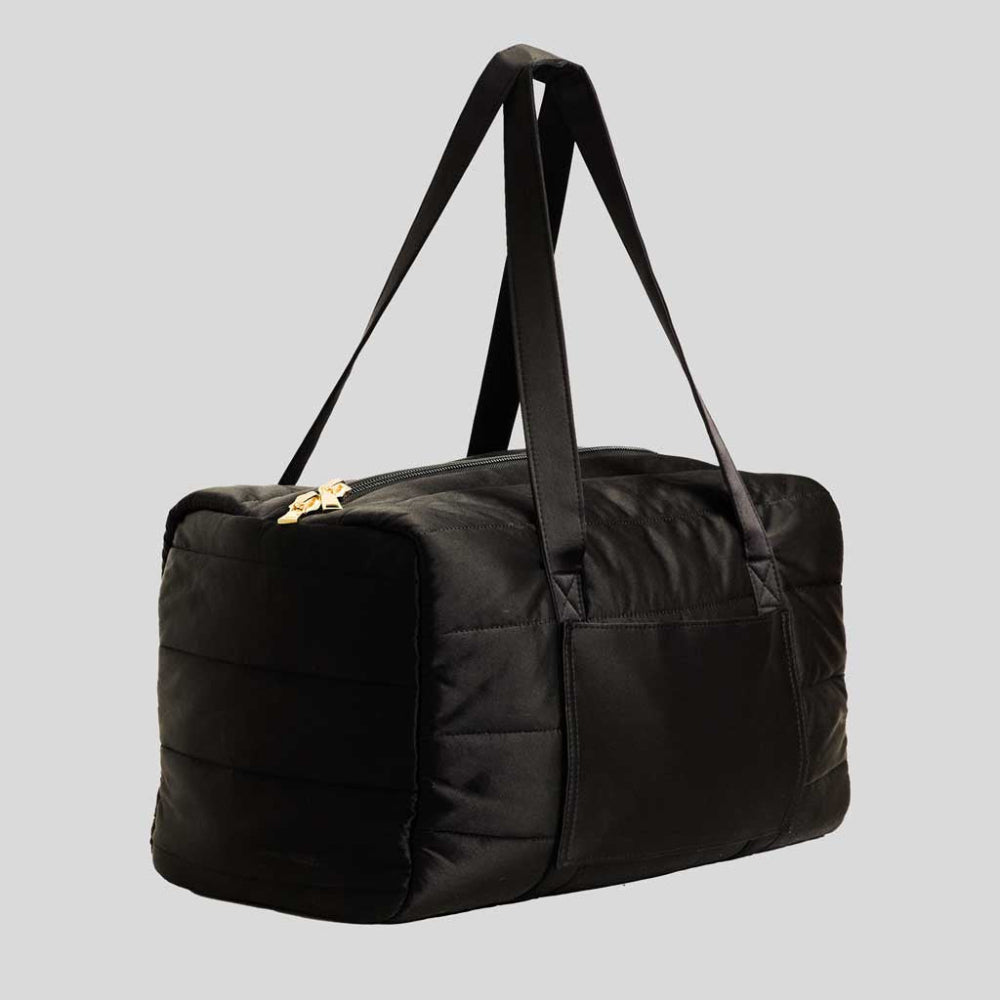 Black duffel bag with a gold zipper on a light grey background. Travel bag.