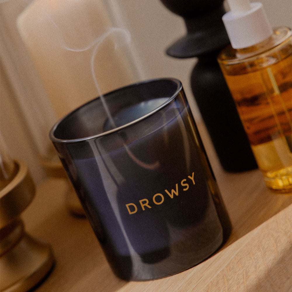 Black candle labelled 'Drowsy' with a small bottle of oil on a wooden surface.