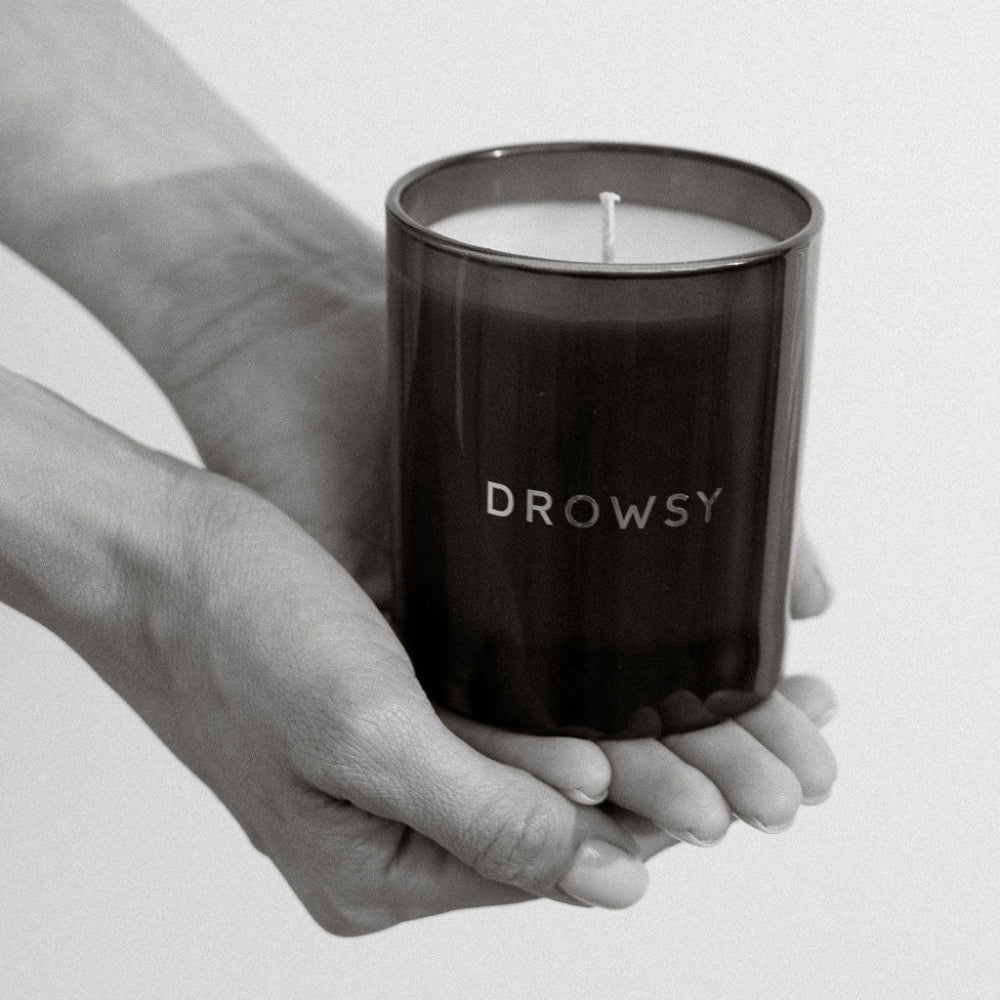 Hand holding a black candle labelled 'Drowsy' against a light background
