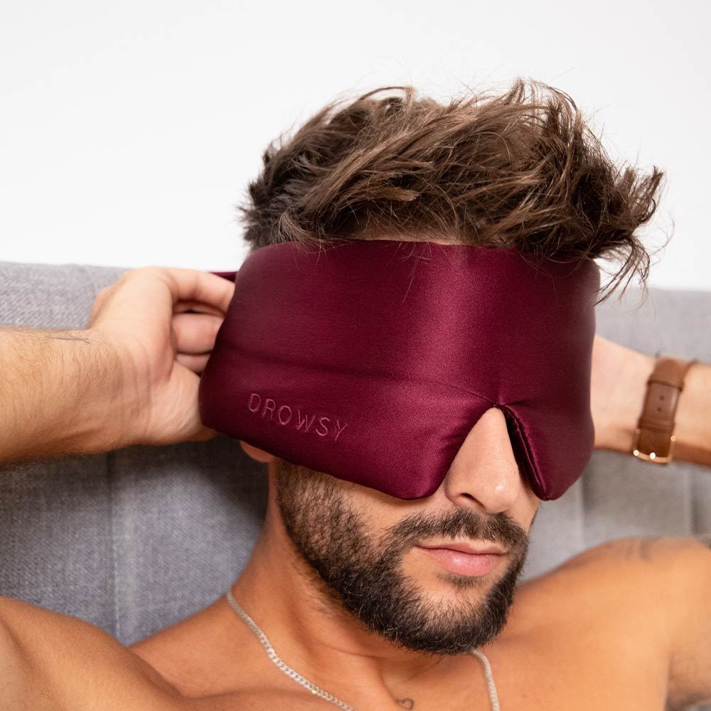Person wearing a burgundy sleep mask while lying on a couch.