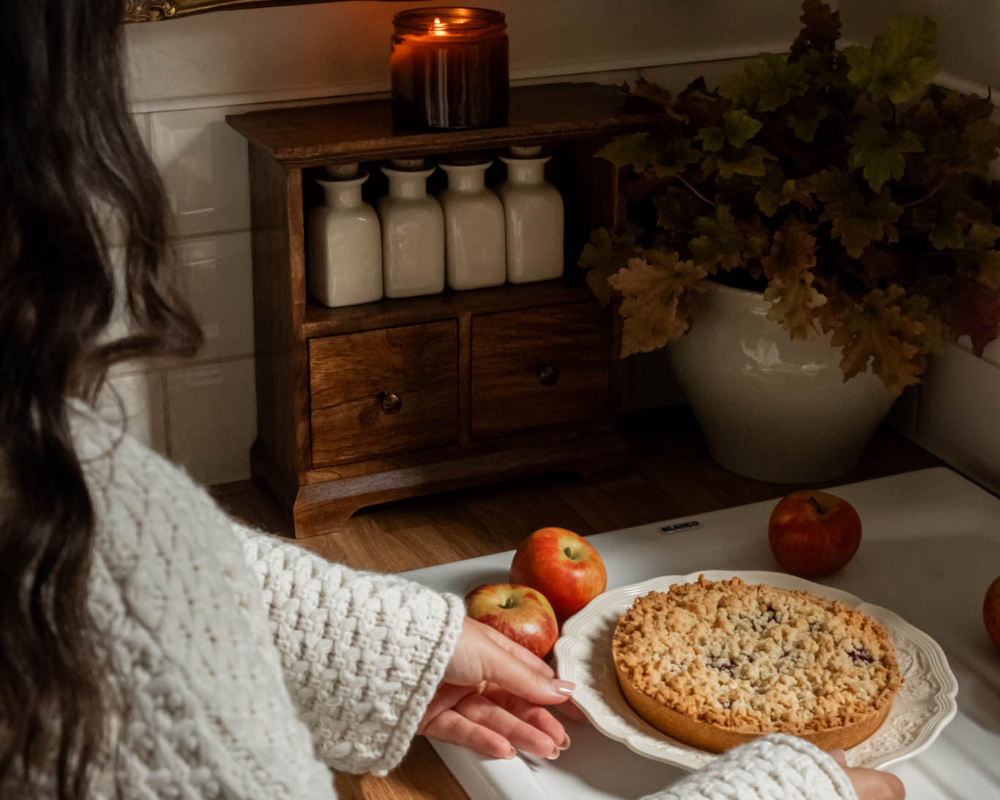 Person holding a plate with a crumble dessert in a cosy kitchen setting.