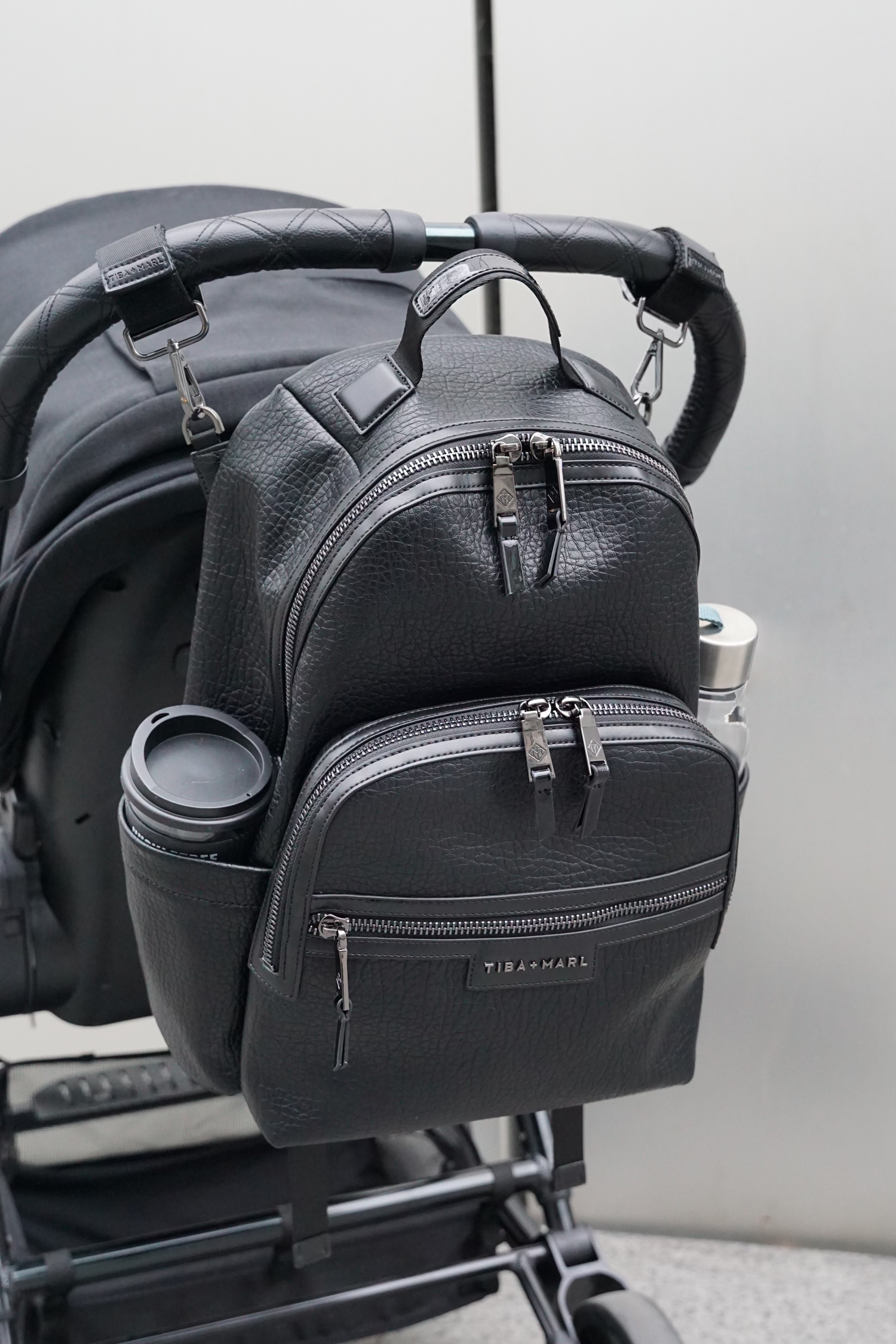 Black backpack attached to a stroller with a neutral background
