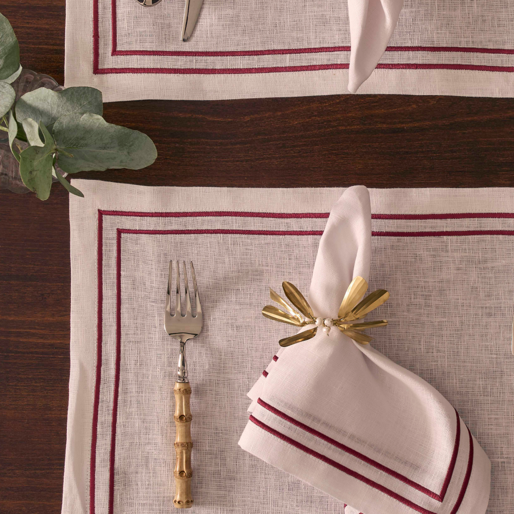 Table setting with a gold napkin ring, white napkin, and fork on a red-striped placemat.