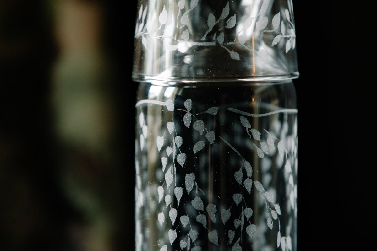 Clear glass tumbler with floral etching on a dark background