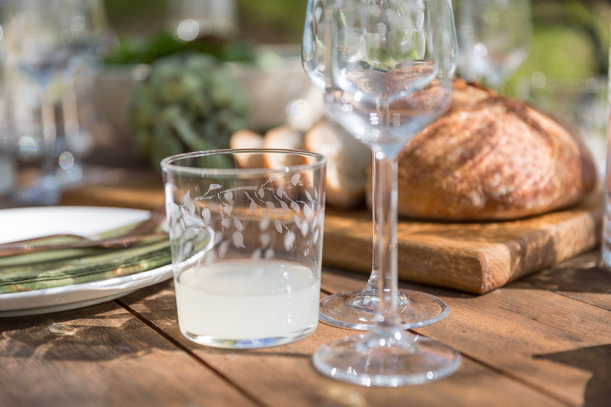 Wine glass and glass tumbler on a wooden table with bread in the background