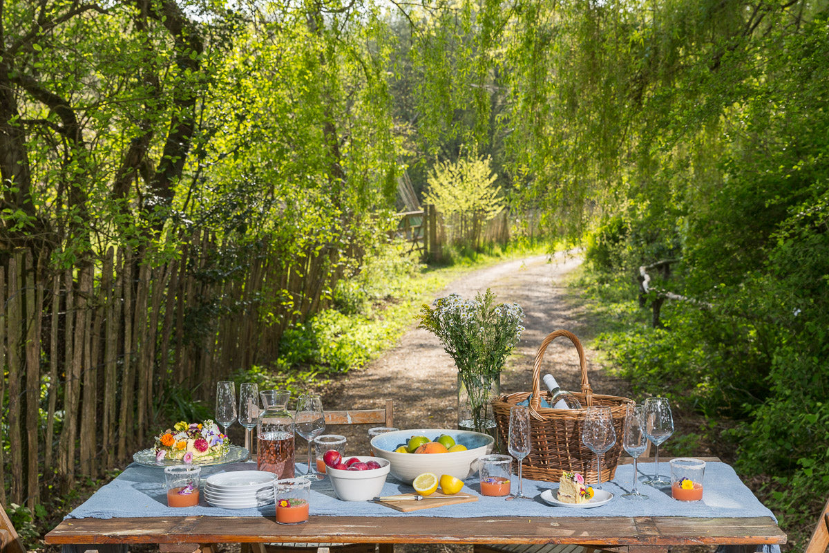 Outdoor dining setup with table, chairs, and picnic basket in a garden.