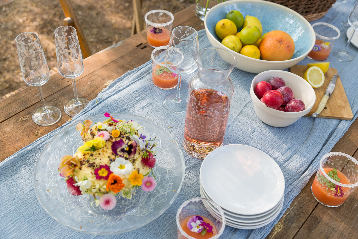 Outdoor table setting with flowers, plates, and drinks on a wooden table.