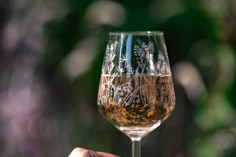 Wine glass with nature-themed engraving held against a blurred natural background