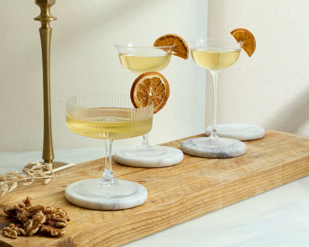 Three cocktails with orange slices on a wooden board with a neutral background on round white and grey marble coasters
