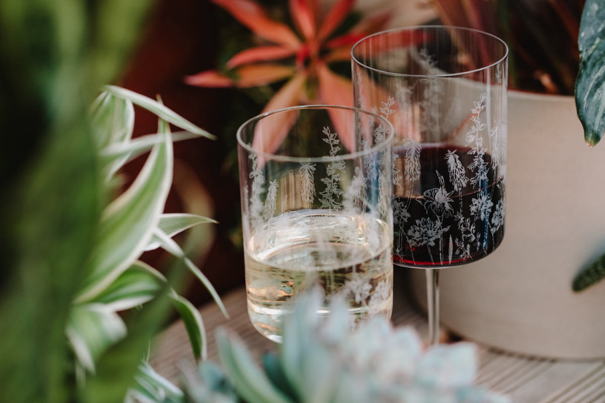 Two glasses, one filled with champagne and the other with red wine, on a table with plants in the background.
