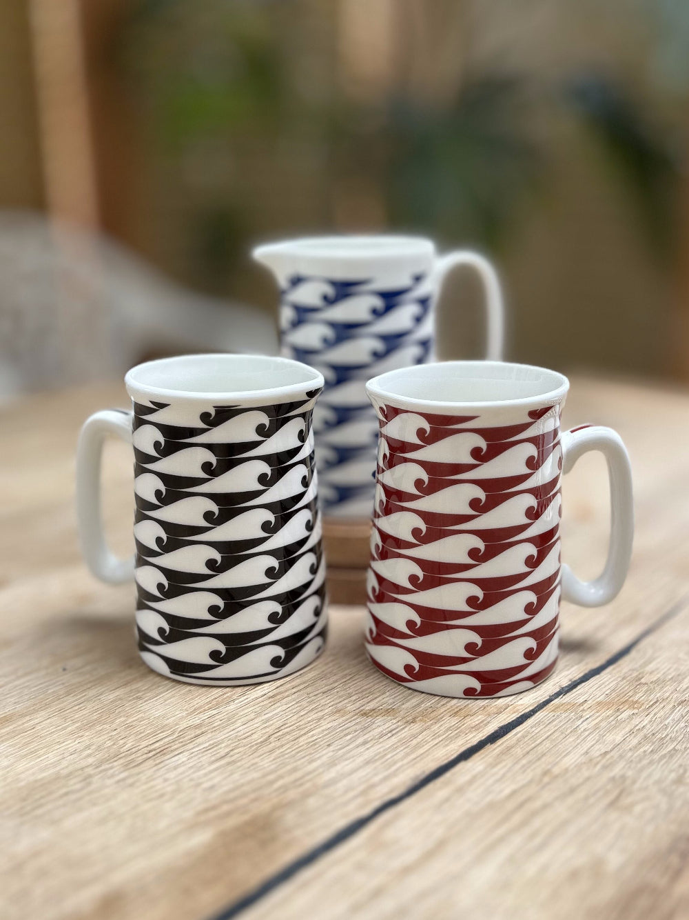 Three ceramic mugs Red Blue and Black with wave patterns on a wooden surface