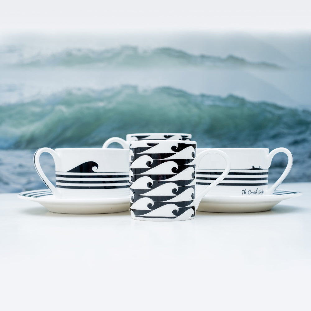 Ceramic cups and saucers with wave design against a blurred ocean background