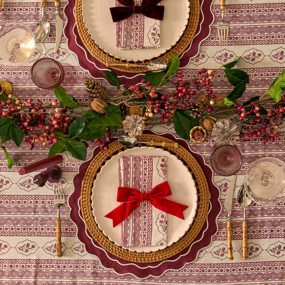 Decorative table setting with plates, napkins, and red bows on a patterned tablecloth.