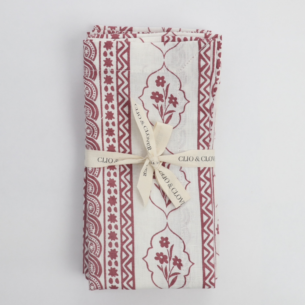 Folded linen napkin with red patterns and a white ribbon on a light grey background