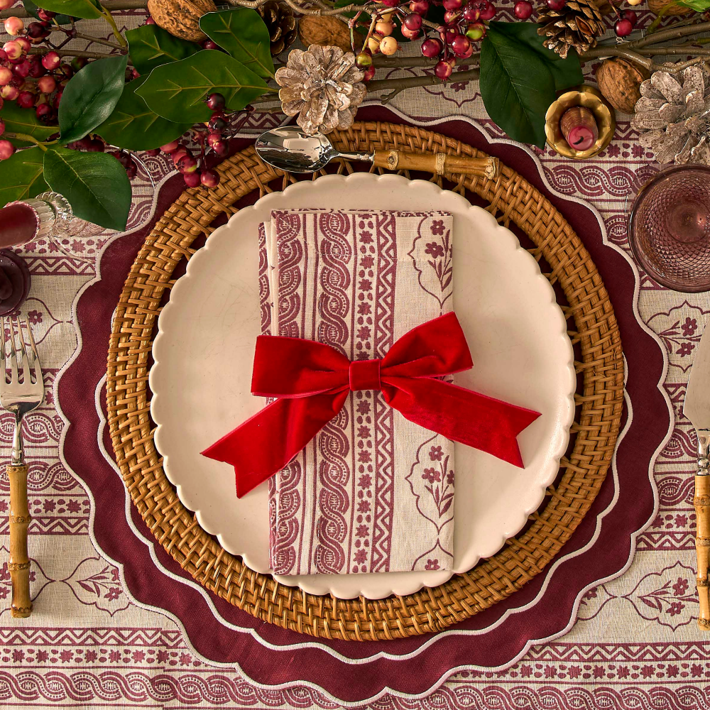 Decorative table setting with a plate, napkin, and red bow on a patterned tablecloth.