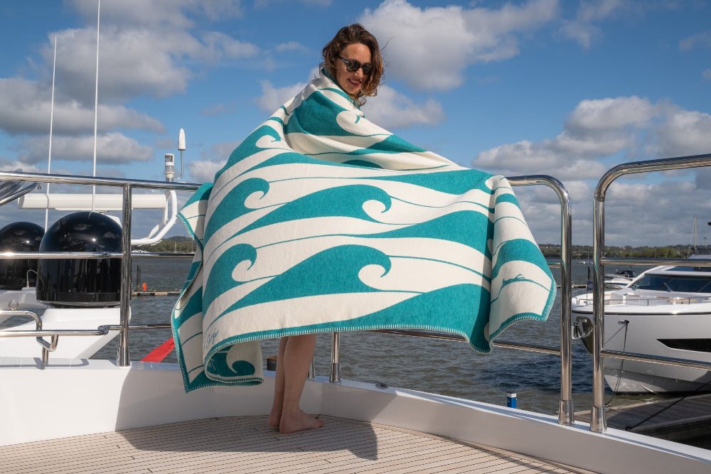 Person holding a teal and white wave-patterned towel on a boat deck with water and sky in the background