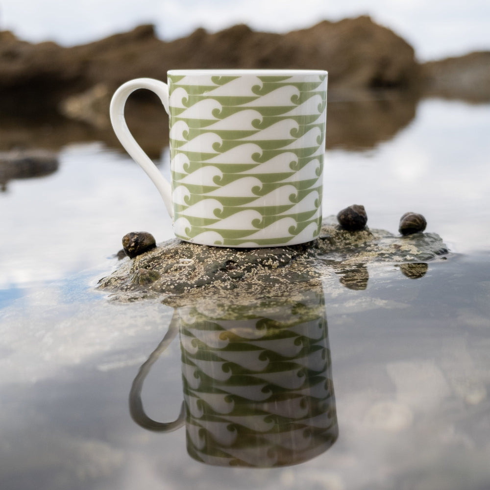 Green and white Mug with wave pattern on a rock by water