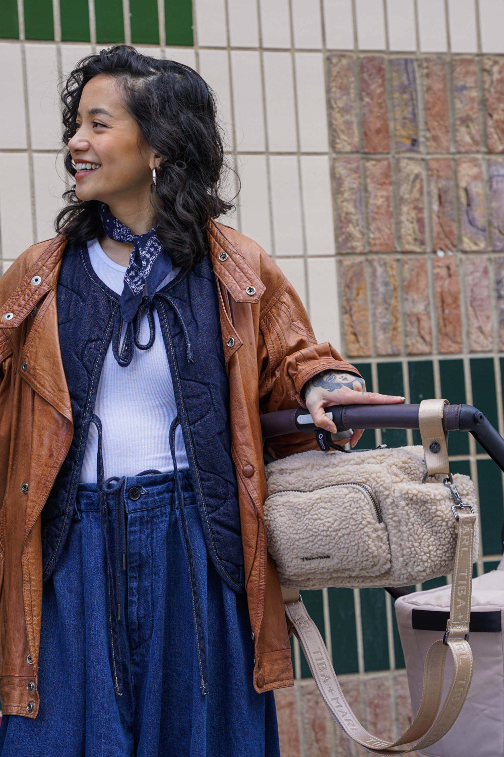 Person holding a beige fleece bag clipped to baby buggy handle outside