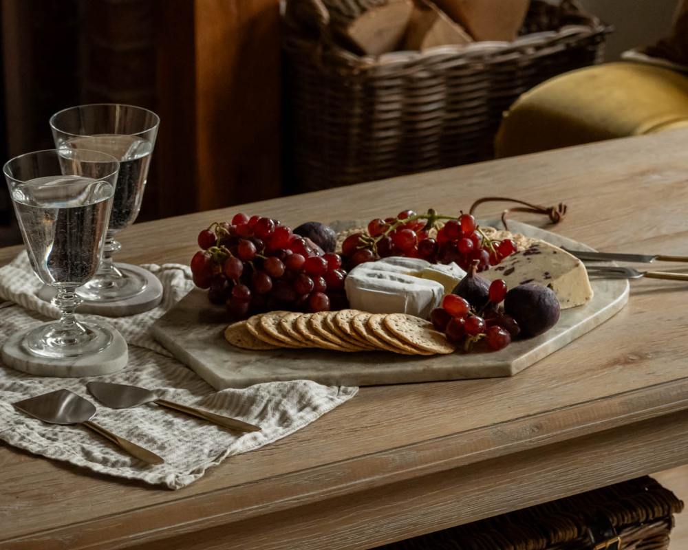 Wooden table with a cheeseboard featuring grapes, crackers, and cheese, accompanied by water glasses.