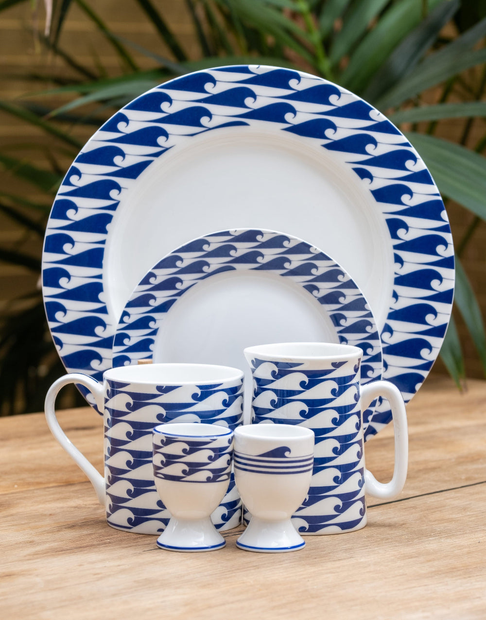 Ceramic tableware set with blue and white wave pattern on a wooden surface.
