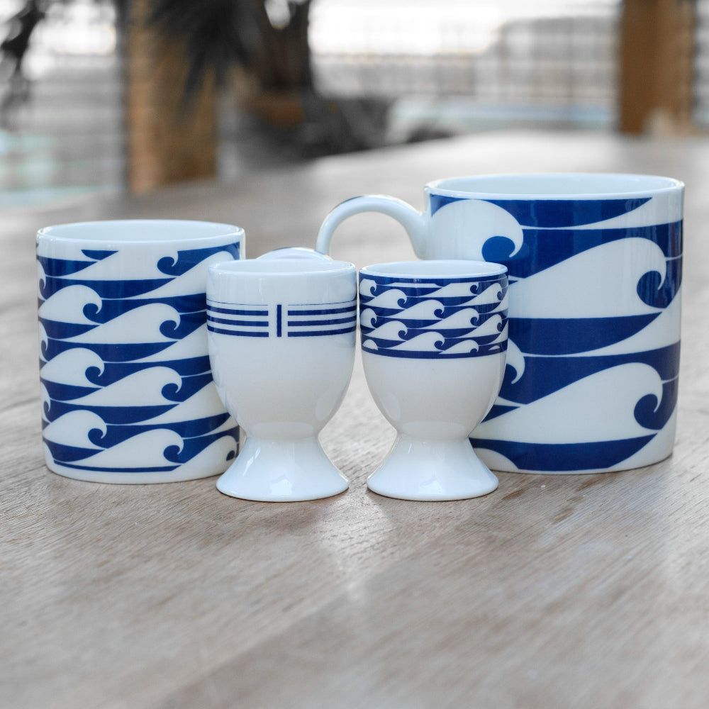 Set of ceramic cups and egg cups with blue wave patterns on a wooden surface