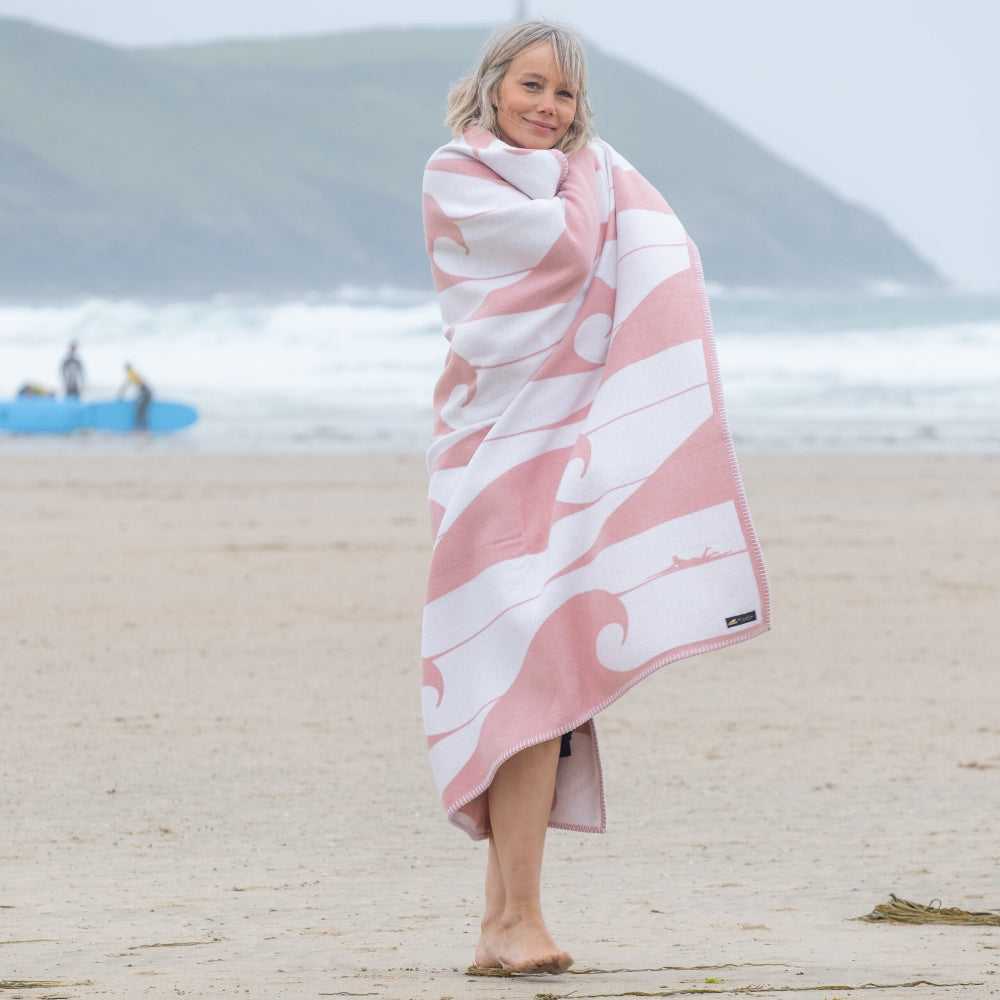 Woman wrapped in a pink and white patterned towel on a beach with mountains in the background